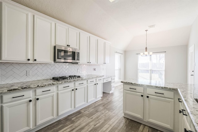 kitchen featuring white cabinets, lofted ceiling, appliances with stainless steel finishes, light wood-style floors, and backsplash