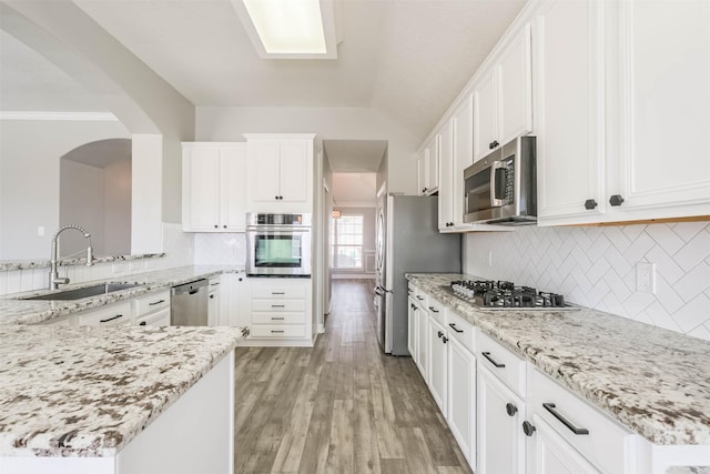 kitchen featuring stainless steel appliances, a sink, light stone countertops, and light wood-style floors