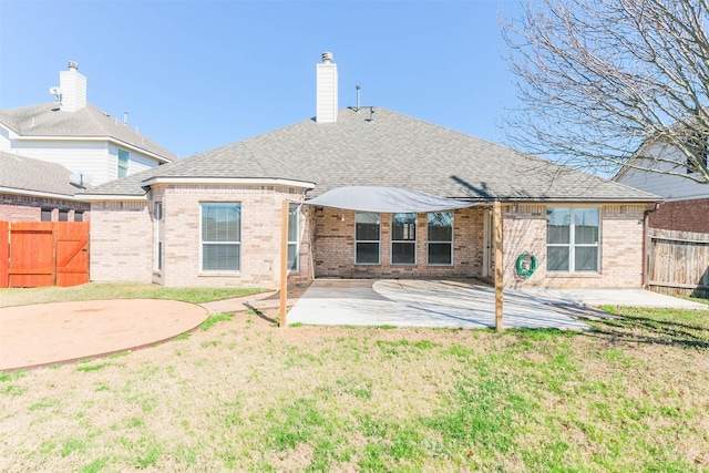 rear view of property with fence, a yard, roof with shingles, a chimney, and a patio area