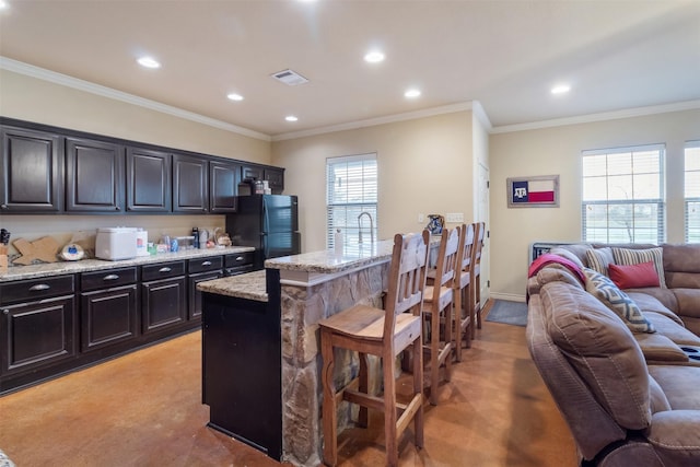 kitchen featuring light stone counters, a breakfast bar area, visible vents, open floor plan, and freestanding refrigerator