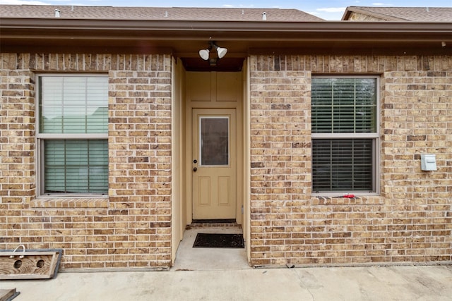 entrance to property with roof with shingles and brick siding