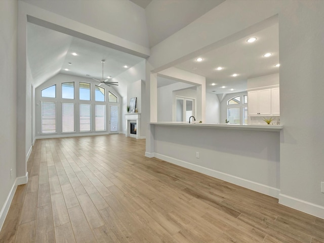 unfurnished living room featuring light wood-type flooring, a healthy amount of sunlight, ceiling fan, and a warm lit fireplace