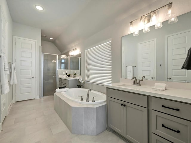 bathroom featuring two vanities, vaulted ceiling, a stall shower, a bath, and a sink