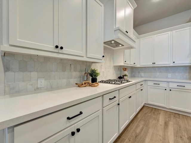 kitchen featuring light wood-type flooring, white cabinetry, stainless steel gas stovetop, light countertops, and decorative backsplash