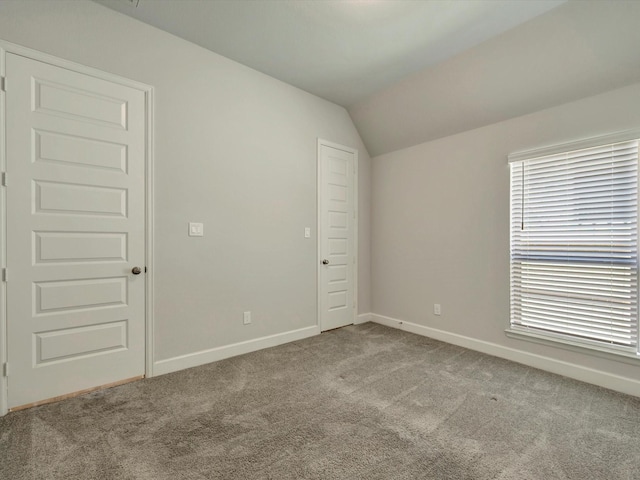 carpeted empty room featuring vaulted ceiling and baseboards