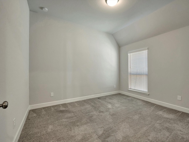 carpeted empty room with baseboards and vaulted ceiling