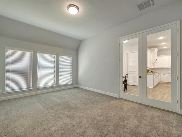 spare room with visible vents, baseboards, lofted ceiling, french doors, and light colored carpet