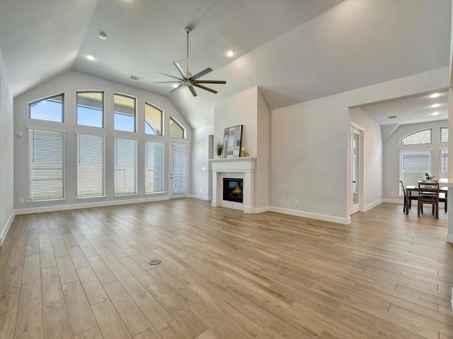 unfurnished living room with lofted ceiling, a ceiling fan, a glass covered fireplace, light wood-style floors, and baseboards