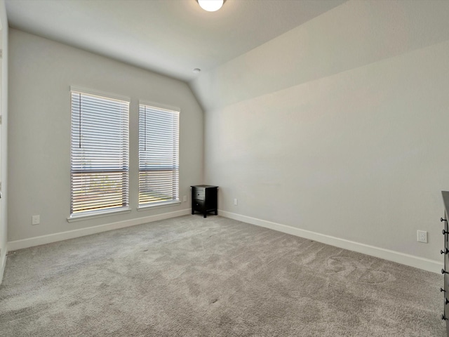 carpeted empty room with baseboards and vaulted ceiling