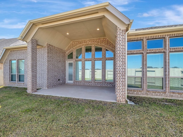 doorway to property with a yard, a patio, and brick siding