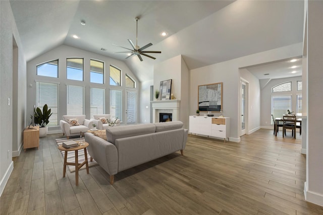 living room with baseboards, ceiling fan, wood finished floors, a glass covered fireplace, and high vaulted ceiling