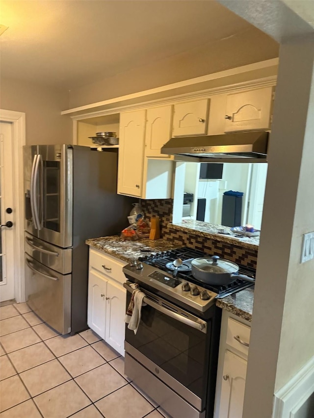 kitchen with light tile patterned flooring, under cabinet range hood, white cabinetry, appliances with stainless steel finishes, and decorative backsplash