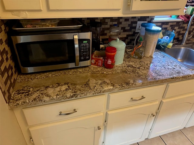 kitchen featuring a sink, stainless steel microwave, decorative backsplash, and white cabinets