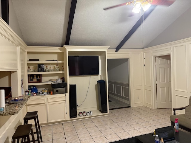 kitchen featuring light tile patterned floors, vaulted ceiling with beams, a decorative wall, a ceiling fan, and open shelves