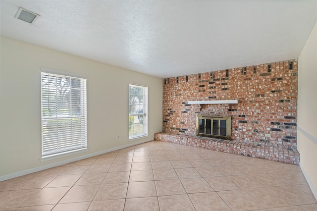 unfurnished living room featuring a brick fireplace, visible vents, a textured ceiling, and tile patterned floors