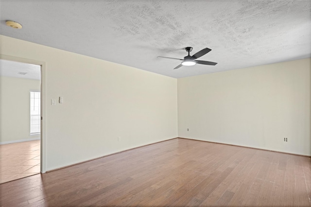 empty room with ceiling fan, a textured ceiling, baseboards, and wood finished floors