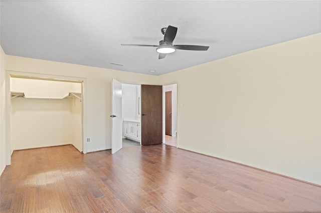 unfurnished bedroom featuring ceiling fan, connected bathroom, wood finished floors, a closet, and a walk in closet