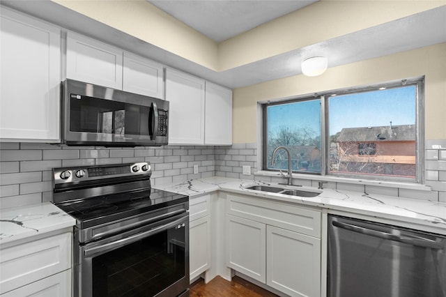 kitchen with stainless steel appliances, a sink, white cabinetry, and decorative backsplash