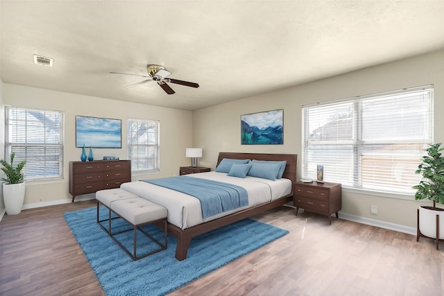 bedroom featuring baseboards, multiple windows, visible vents, and wood finished floors