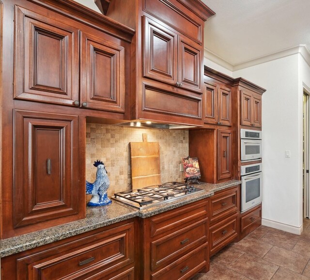 901 Longmire Rd Unit 17, Conroe, TX 77304 - kitchen with decorative backsplash, stainless steel gas stovetop, baseboards, light stone counters, and brown cabinetry