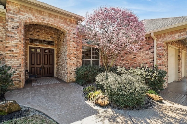 property entrance with a garage, brick siding, and roof with shingles