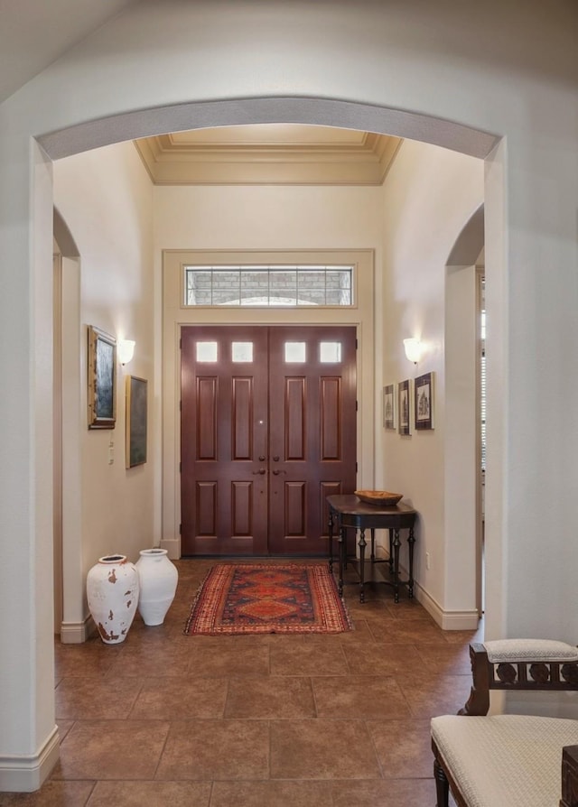 entryway featuring ornamental molding, arched walkways, and baseboards