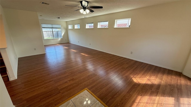 unfurnished living room with baseboards, visible vents, a ceiling fan, dark wood-style flooring, and a textured ceiling