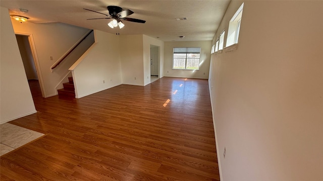 unfurnished living room with ceiling fan, wood finished floors, visible vents, baseboards, and stairs