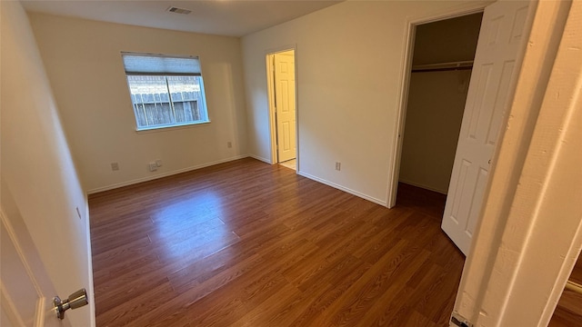 unfurnished bedroom featuring a closet, dark wood-style flooring, visible vents, and baseboards