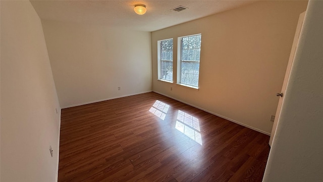 unfurnished room with dark wood-style floors, visible vents, and baseboards