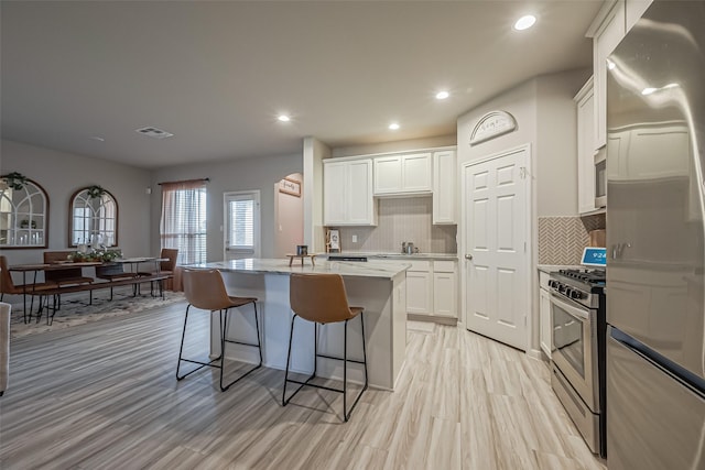 kitchen featuring a kitchen island, visible vents, white cabinets, appliances with stainless steel finishes, and a kitchen bar