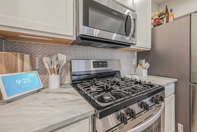 kitchen with appliances with stainless steel finishes, backsplash, light stone countertops, and white cabinets