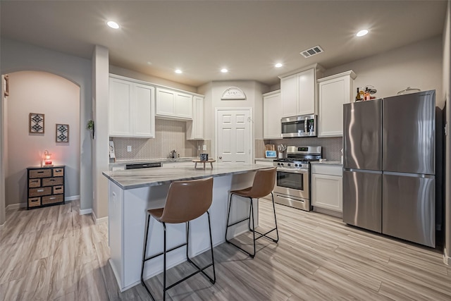 kitchen featuring visible vents, arched walkways, appliances with stainless steel finishes, a breakfast bar area, and white cabinetry