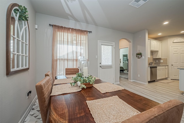 dining room featuring arched walkways, light wood-style flooring, recessed lighting, visible vents, and baseboards