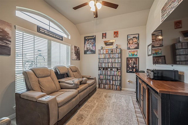 living area featuring a ceiling fan, vaulted ceiling, light wood-style flooring, and baseboards