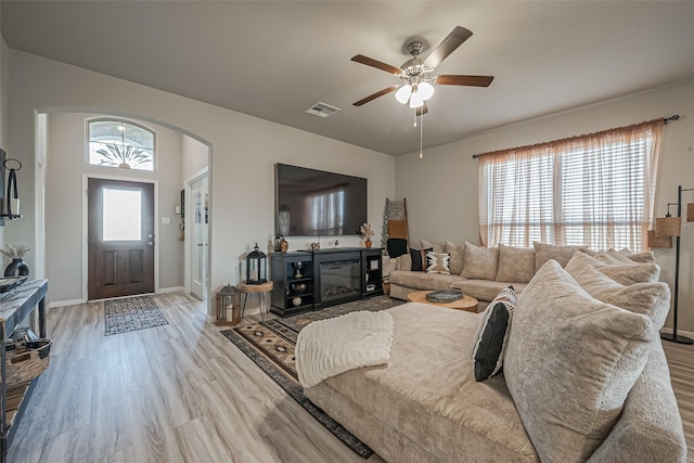 living area with baseboards, visible vents, arched walkways, a ceiling fan, and light wood-style floors