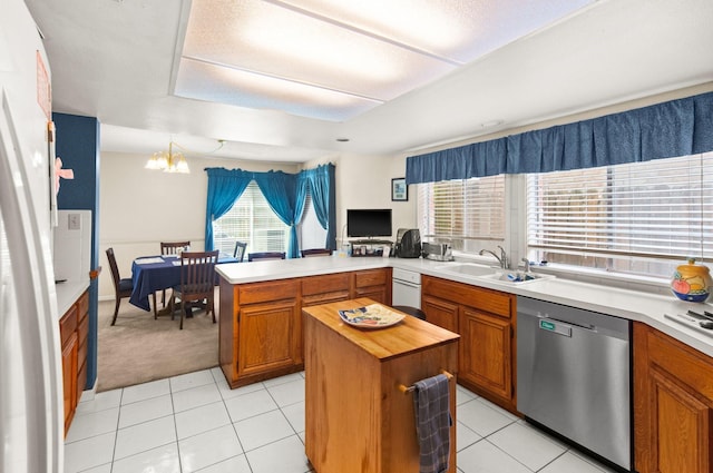 kitchen featuring a sink, stainless steel dishwasher, a peninsula, an inviting chandelier, and light tile patterned floors