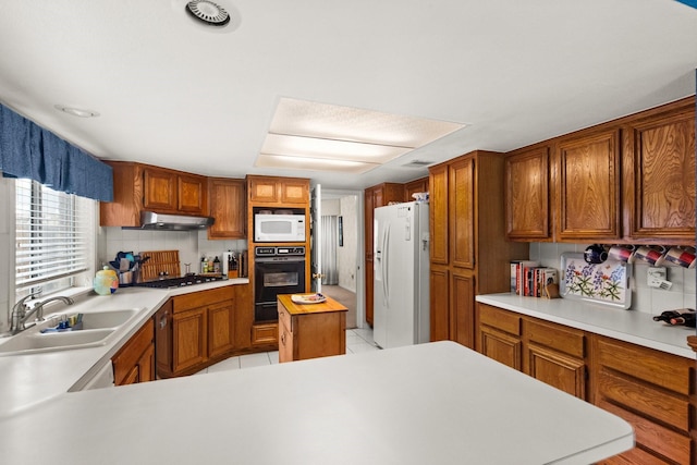 kitchen with a sink, under cabinet range hood, white appliances, light countertops, and decorative backsplash