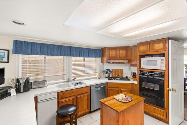 kitchen with light tile patterned floors, stainless steel appliances, a sink, under cabinet range hood, and a warming drawer