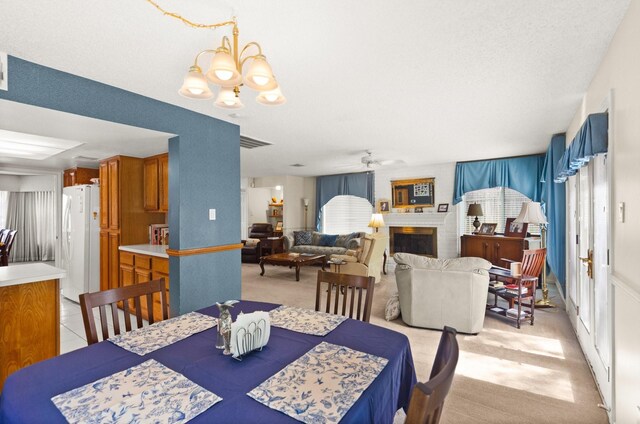 dining area featuring light carpet, visible vents, ceiling fan with notable chandelier, and a fireplace