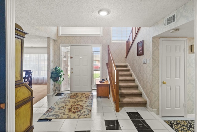 entrance foyer featuring visible vents, a textured ceiling, stairway, wallpapered walls, and light tile patterned floors