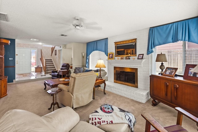 living room with a textured ceiling, carpet flooring, a brick fireplace, ceiling fan, and stairs