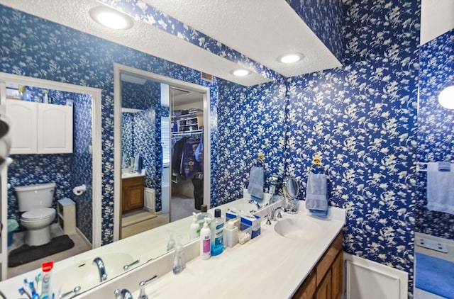 full bath featuring a textured ceiling, toilet, vanity, and wallpapered walls