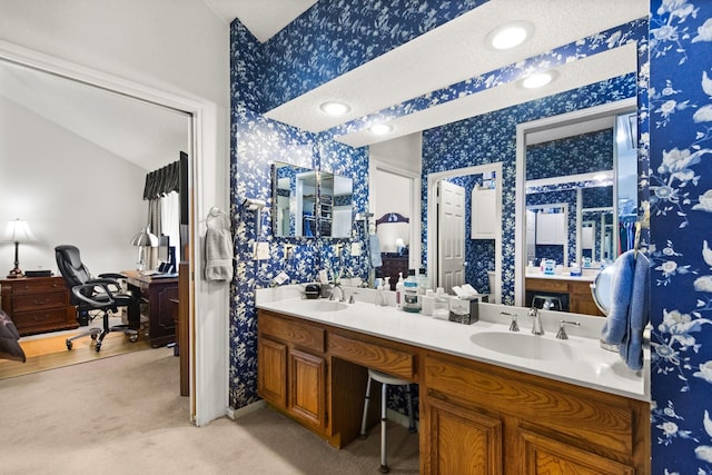 bathroom featuring wallpapered walls, double vanity, vaulted ceiling, and a sink