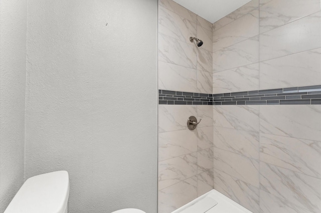 bathroom with toilet, tiled shower, and a textured wall