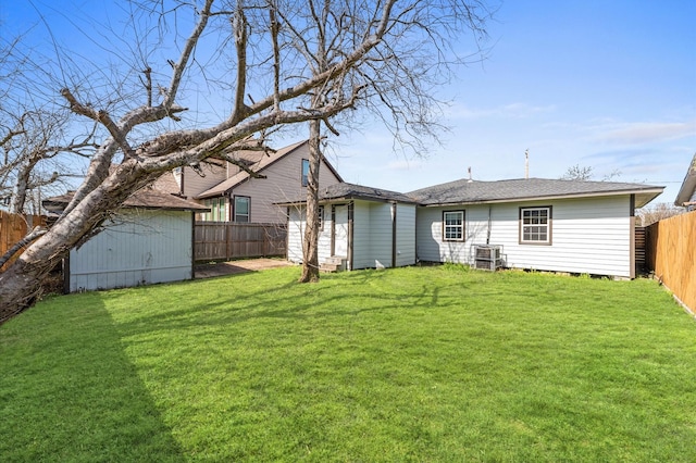 rear view of house featuring an outbuilding, a fenced backyard, a lawn, and a storage unit