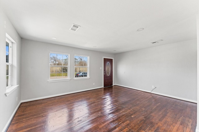 empty room featuring wood-type flooring, visible vents, and baseboards