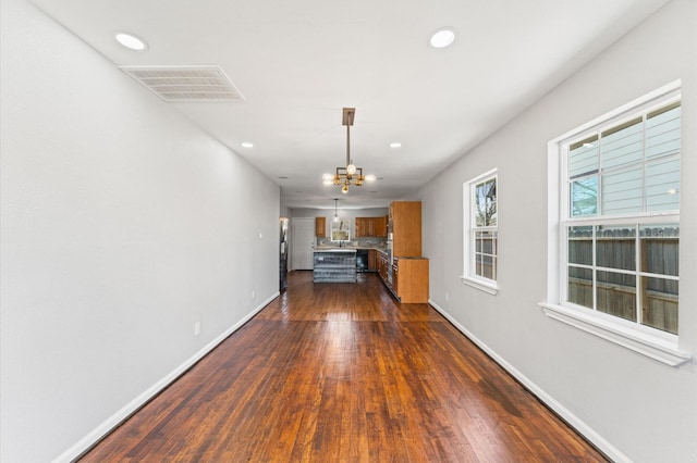 unfurnished living room featuring an inviting chandelier, dark wood finished floors, visible vents, and baseboards