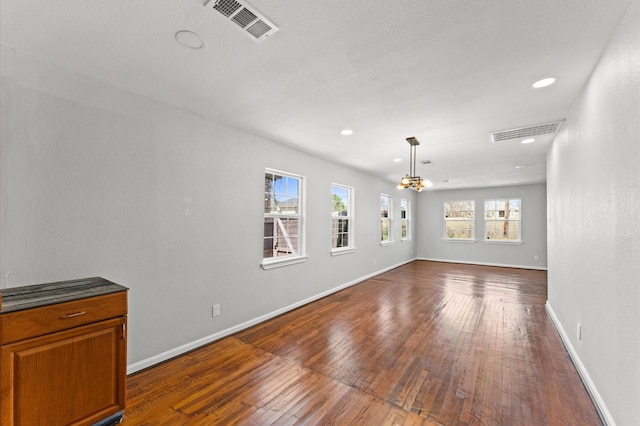 empty room with baseboards, a notable chandelier, visible vents, and dark wood-type flooring