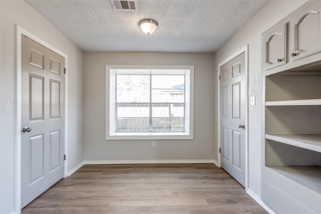 interior space with a textured ceiling, light wood-style flooring, visible vents, and baseboards